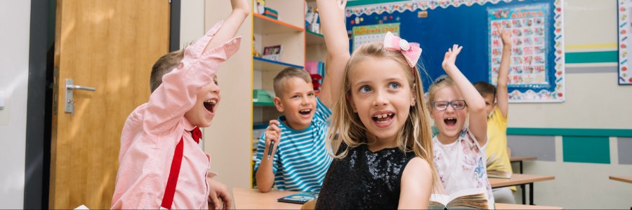 Smiling kids raising hands in class